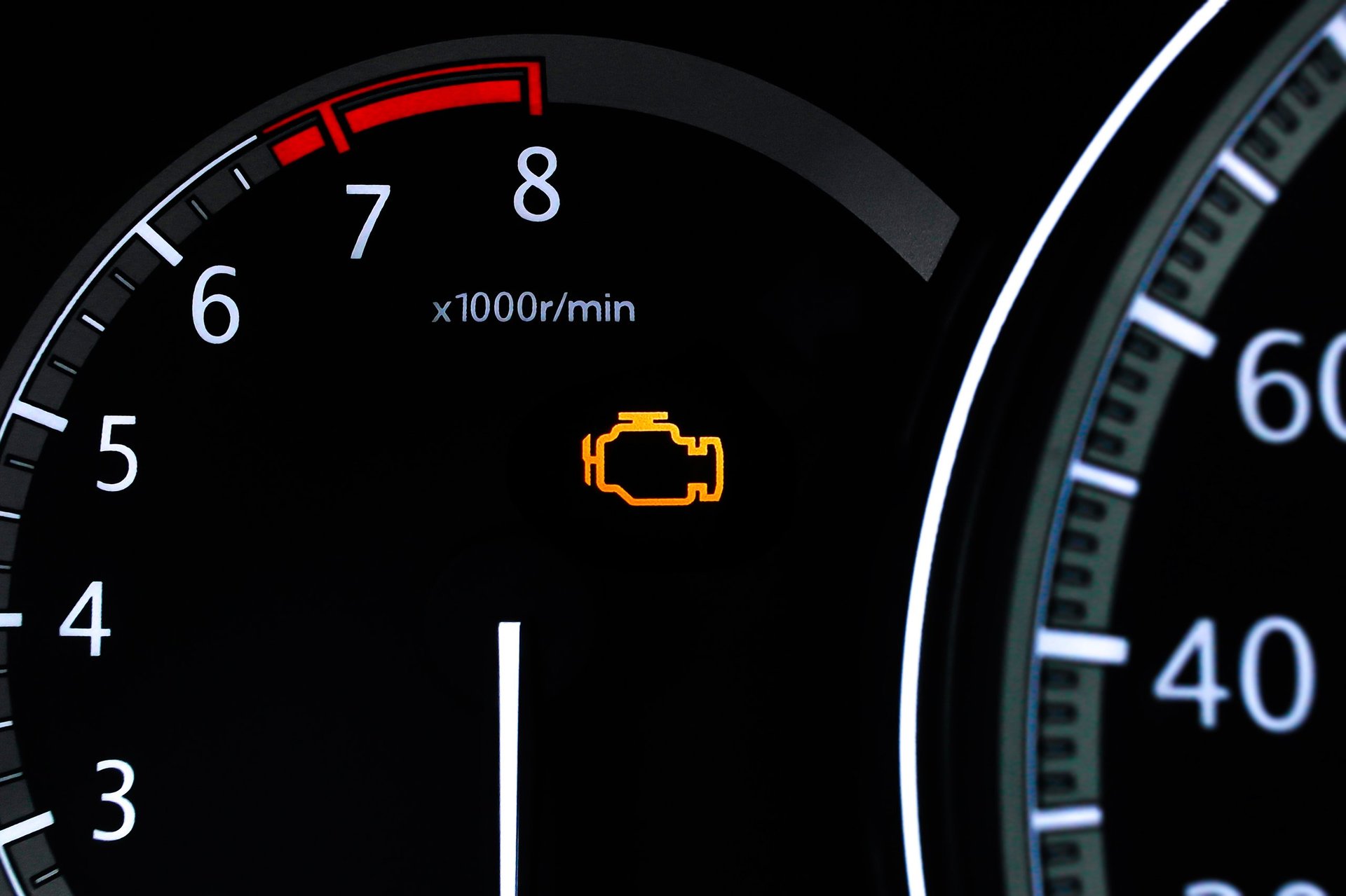 Closeup of a car dashboard with an illuminated check engine light and the tachometer displaying engine revolutions per minute